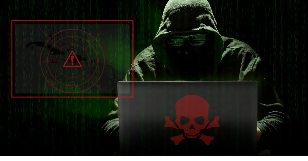 Hacker in dark hoodie using laptop with red skull icon, symbolizing ransomware threats targeting Caribbean businesses